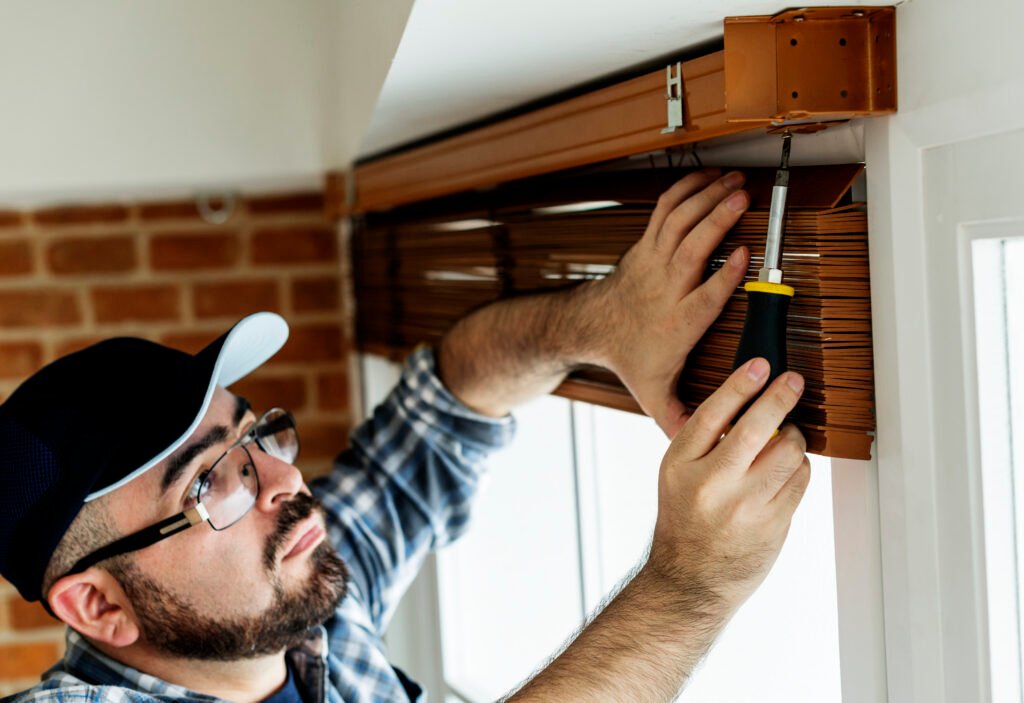A man carefully installing blinds on a window frame, using a screwdriver. Step-by-step guidance on how to install blinds.